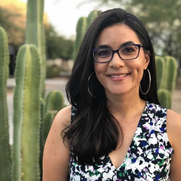 Portrait of ASU Associate Professor Vanessa Fonseca-Chávez. Fonseca-Chávez is smiling, has long, dark hair and is wearing glasses. Cacti are in the background.