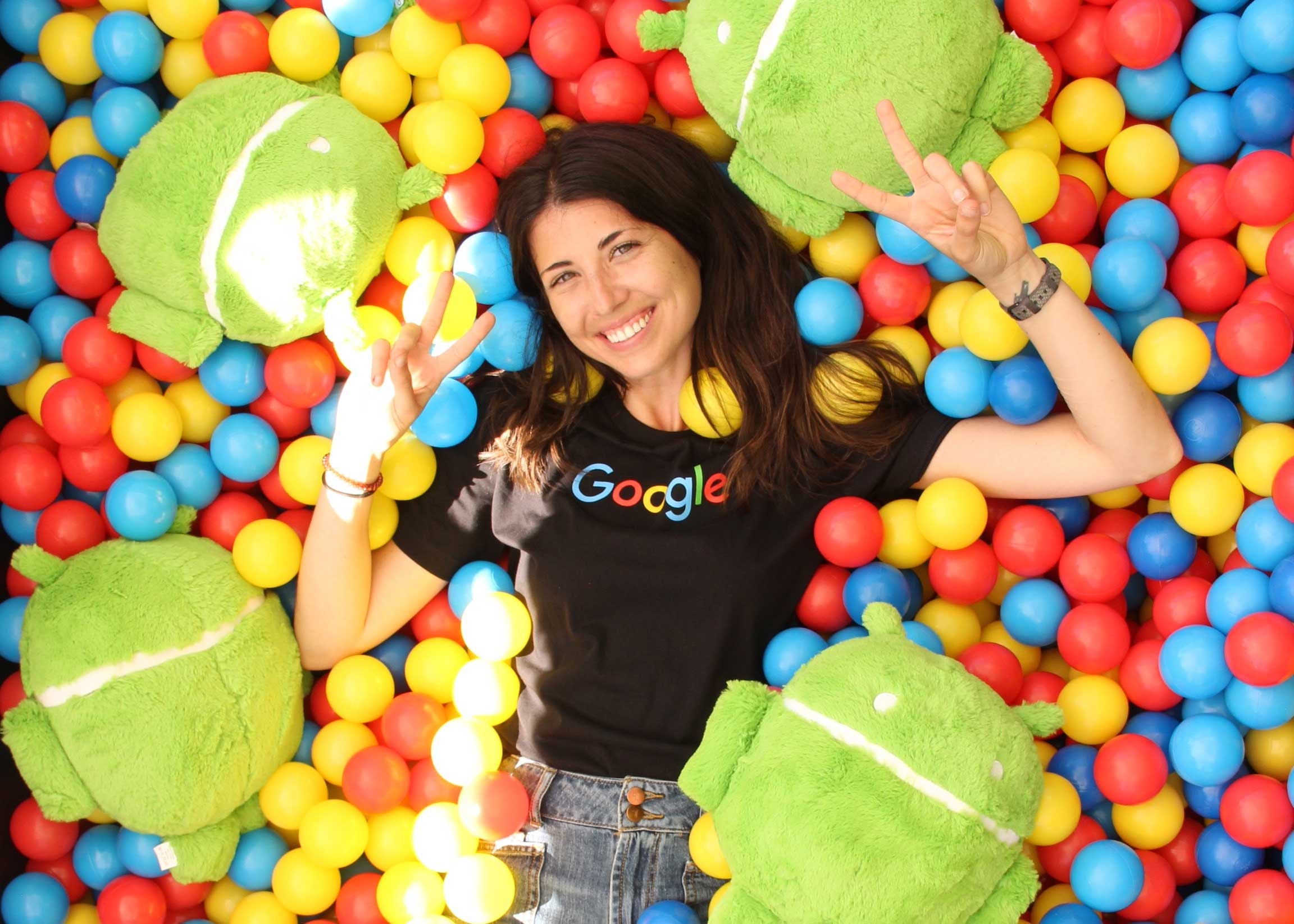 Graduating doctoral student, Jeri Sasser, holds two peace signs up with her hands while wearing a Google shirt against a Google-branded background.
