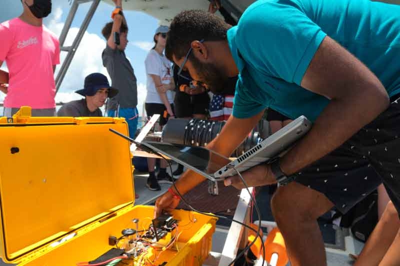 Grad student checks drone equipment on a boat