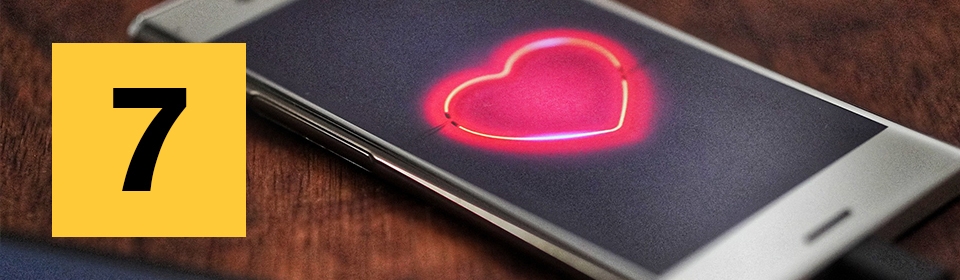 A smart phone on a table with a heart icon in the center of the screen.