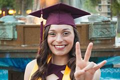 woman in grad cap giving pitchfork sign with hand in front of fountain