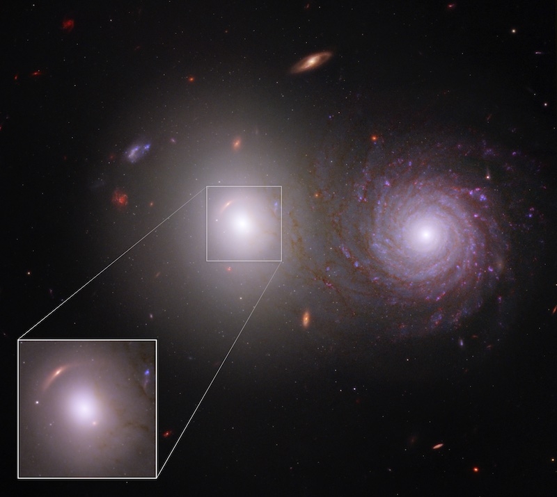 The majority of the image shows the black background of space. Two large, very bright galaxies dominate the center of the image. At right is a bright spiral galaxy. It also has a bright white core, but has red and light purple spiral arms that start at th