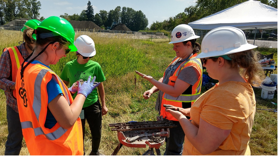 Student researchers pictured doing work in a field, wearing hard hats and orange vests.