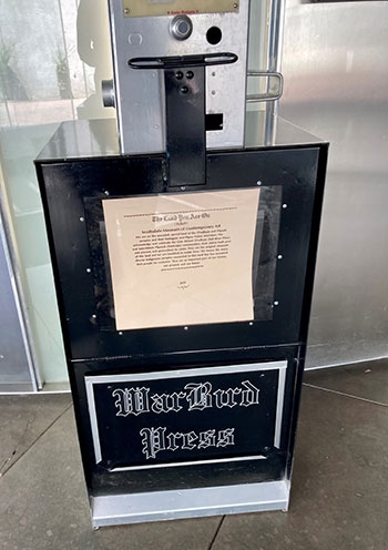 A newspaper vending machine holds printed material with a land acknowledgement 