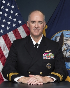 Scott Ruston posing in uniform with flags behind him.