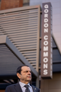 Photo of man in suit in front of building with a sign that says Gordon Commons