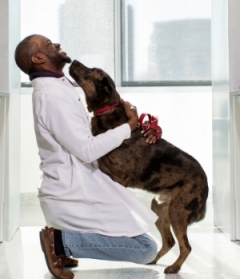 Black man in lab coat hugging dog 