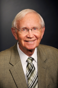 Lonnie Ostrom wears a brown suit and smiles for his headshot