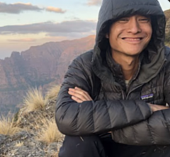 ASU researcher Kenny Chiou smiles while wearing a black coat with the hood up. A view of mountains and clouds can be seen in the background.