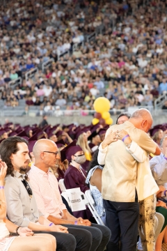 A man and woman embrace in front of a crowd of graduating students