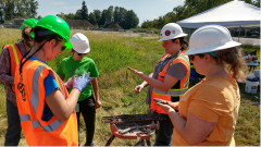 Student researchers pictured doing work in a field, wearing hard hats and orange vests.