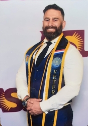 Nick Bedwell poses wearing a veteran stole and smiling against an ASU sign background.