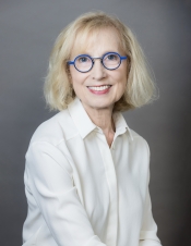 Portrait of woman in white button up blouse, with blonde hair and blue-rimmed glasses