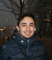 A smiling man wearing a zipped up jacket in the snow.