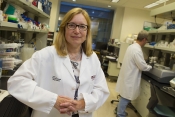 Researcher Karen Anderson, wearing a white lab coat, stands in her laboratory.