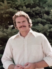 Older photo of man with brown hair and mustache wearing button up white shirt