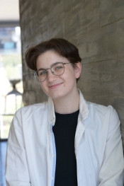 Portrait of a person with short brown hair and glasses wearing a black t-shirt under a white button-down shirt