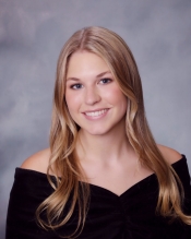 Portrait of a young woman with long blonde hair wearing an off-the-shoulder black garment.