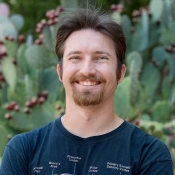 A bearded man smiles in front of a prickly pear cactus.