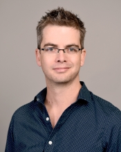 Portrait of a man with short brown hair wearing glasses and a blue button-up shirt