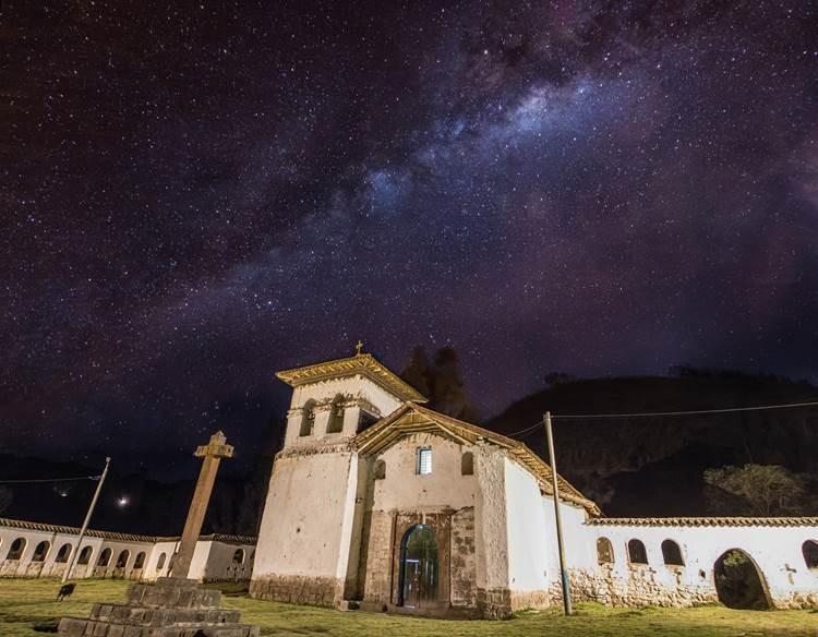A church stands in contrast to a dark night sky with visible stars in the village of Umasbamba in Peru.
