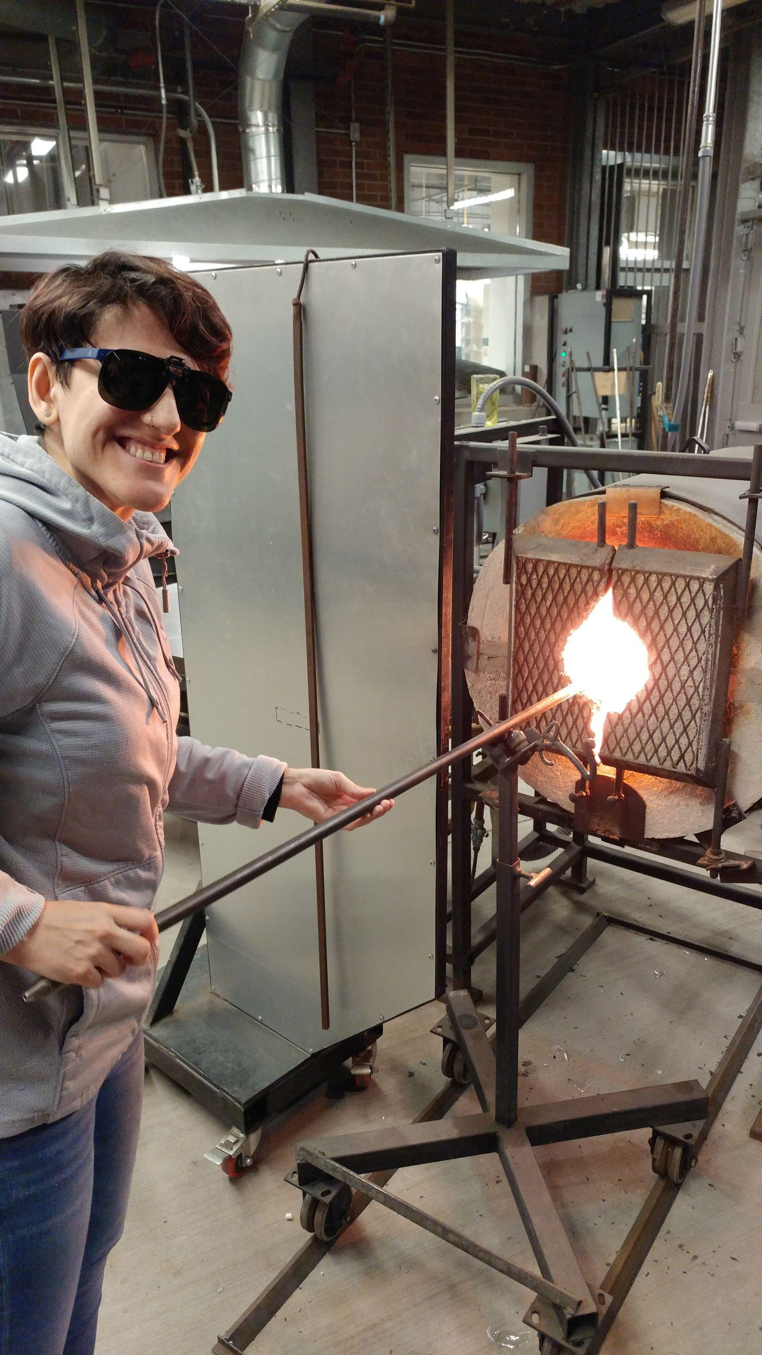 woman putting rod into glass blowing oven