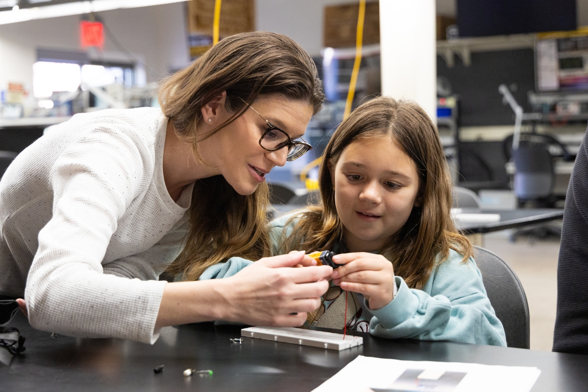 A woman helps a young girl with an engineering hands-on activity