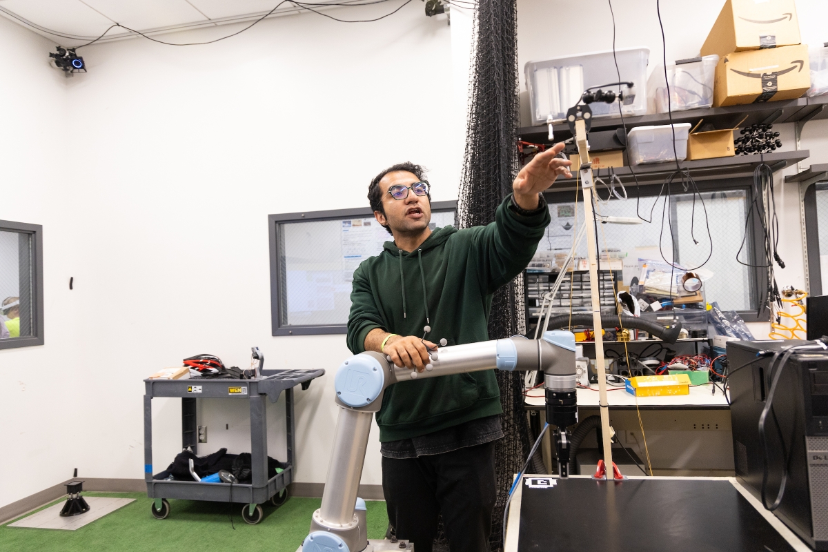 A college student gestures at equipment in an engineering lab
