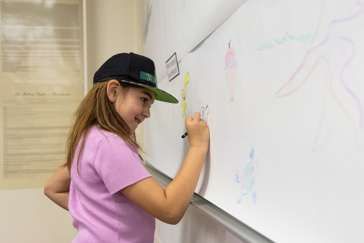 A young girl smiles as she draws on a whiteboard
