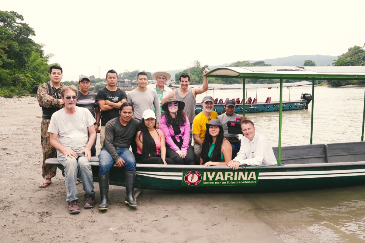 A group of 14 people posing in front of a solar-powered canoe.