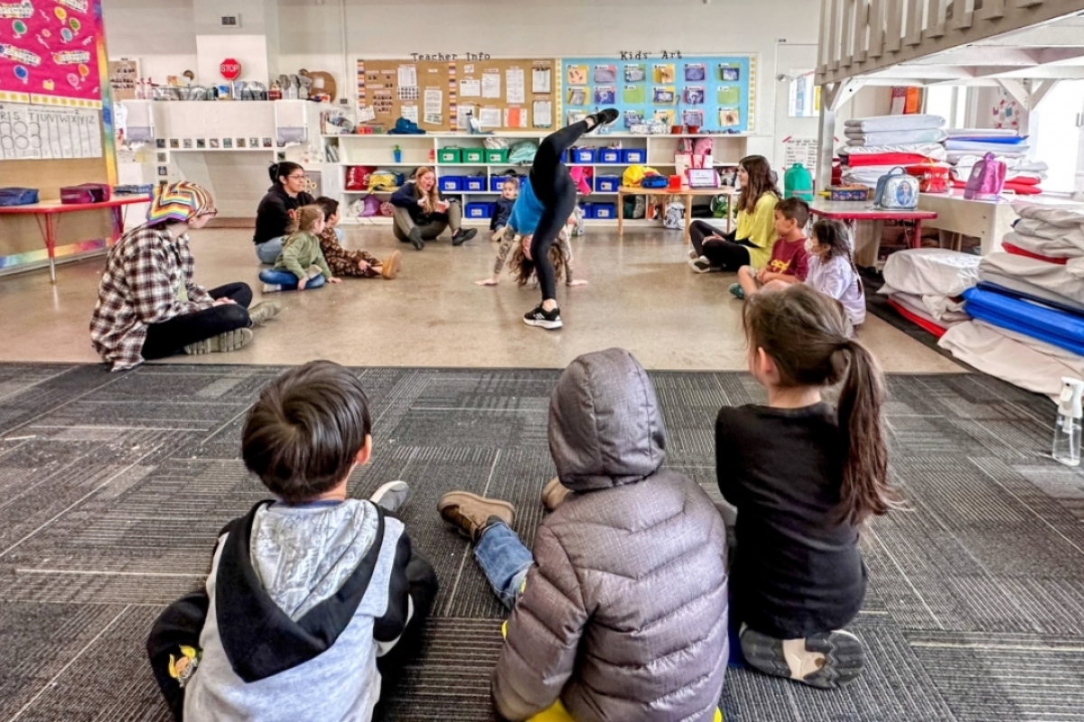Amanda doing a sort of handstand in the middle of a circle of children.