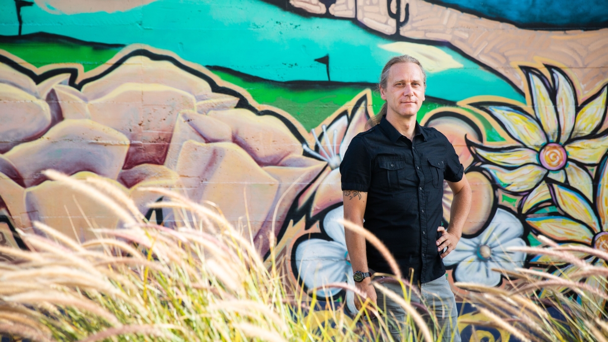 ASU Assistant Professor Tyler Peterson stands in front of a colorful mural in a photo by Deanna Dent.