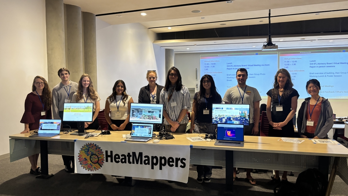 Group of students standing behind a table with computers on it and a sign that reads "HeatMappers."
