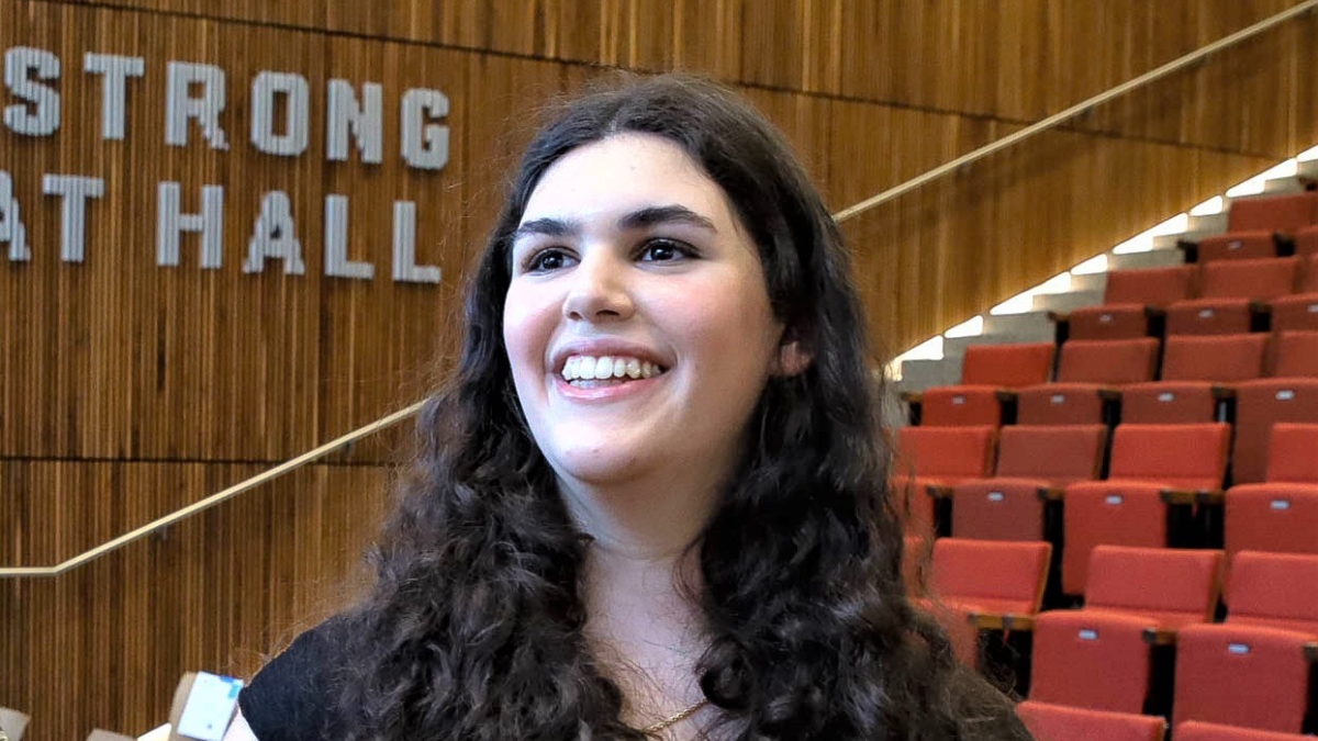 ASU BSN graduate Elliana Tenenbaum smiling and holding a yellow rose in an auditorium.