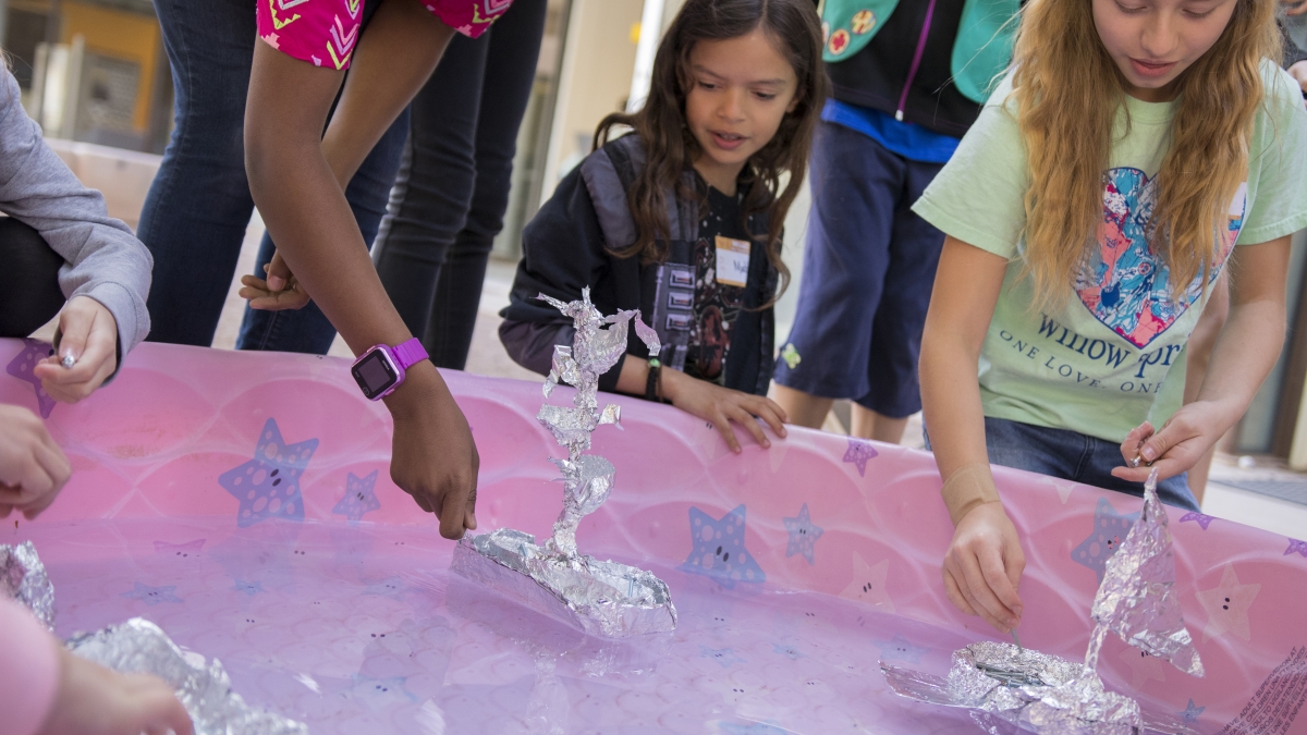 Photo of three girls around a pink pool with foli boats. 