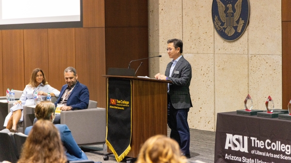 Kenro Kusumi speaking at a podium in front of a seated crowd