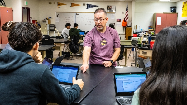 Man sitting at a table opposite two students working on laptops.