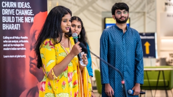 Three students stand in front of a large room full of people.