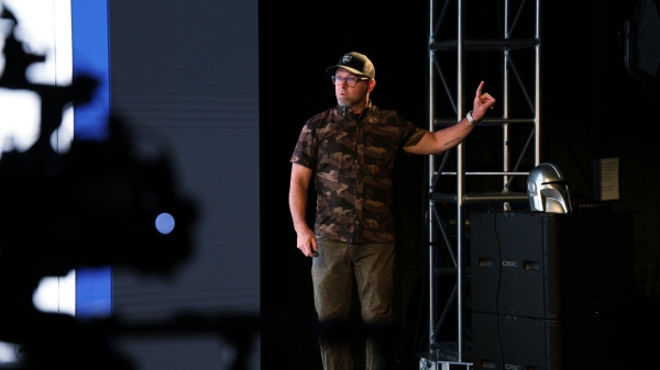 A man in a baseball cap gestures on a soundstage