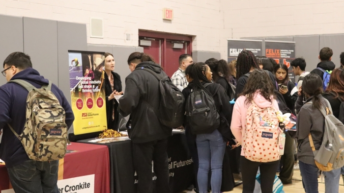 Students walking around a gymnasium with tables with ASU signs.