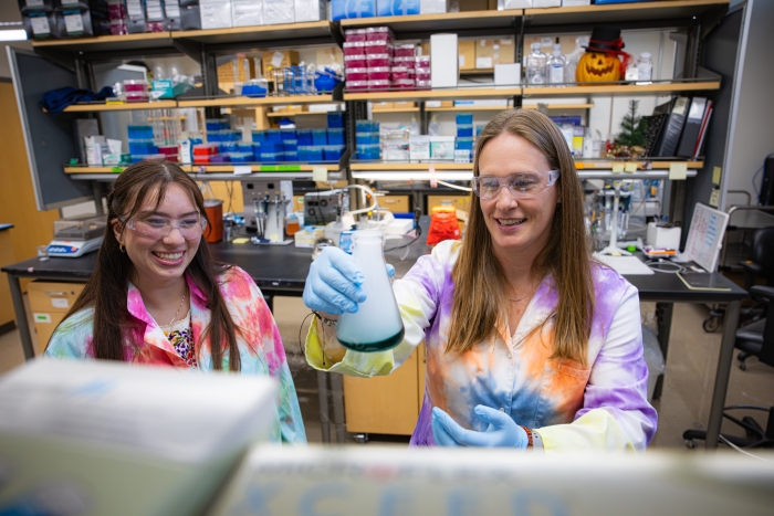 Two women wearing tie-dyed labcoats work in a lab