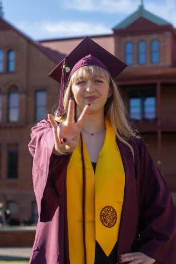 Mia Milinovich stands with a Forks Up hand sign in front of Old Main.