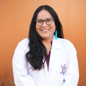 Portrait of a woman with long dark hair wearing black glasses, turquoise earrings and a white lapcoat